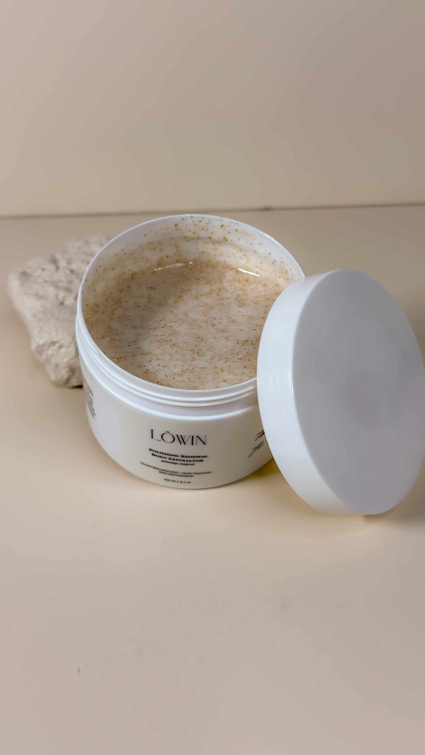 Open jar of Löwin Body Polish product with a white lid on a beige surface
