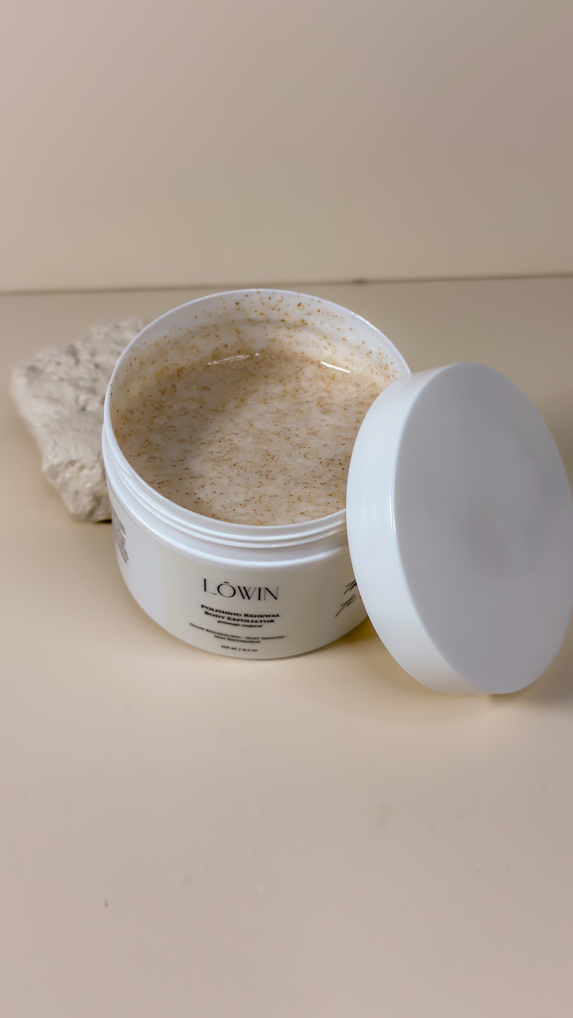 Open jar of Löwin Body Polish product with a white lid on a beige surface