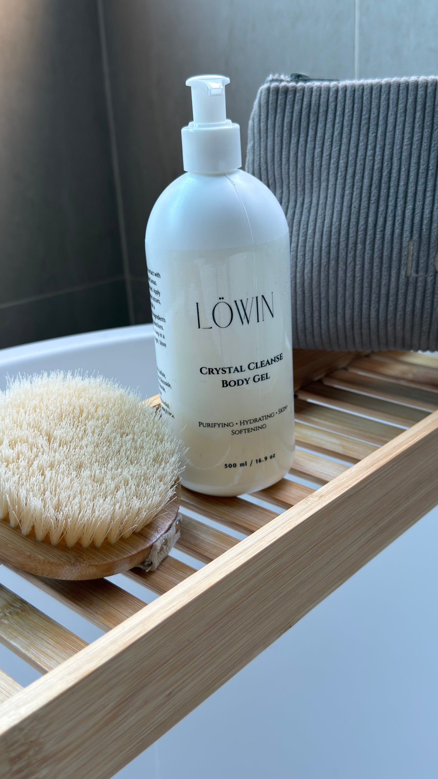 A bottle of Löwin Crystal Cleansing body gel on a wooden bath tray in a bathroom.