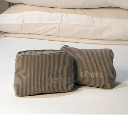 Two corduroy toiletry bags with 'Löwin' branding on a white linen bedding.